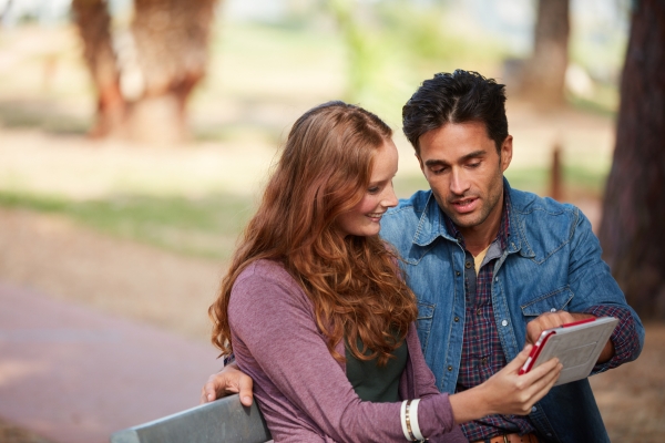 couple watching tablet sitting in park